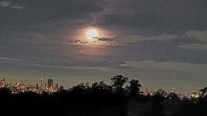 Lua parcialmente encoberta por nuvens sobre cidade iluminada à noite — inspiração para o processo de como escrever haicai.